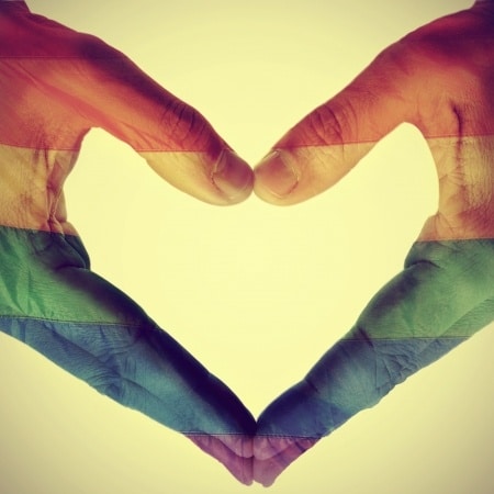picture of man hands forming a hear patterned with the gay pride flag