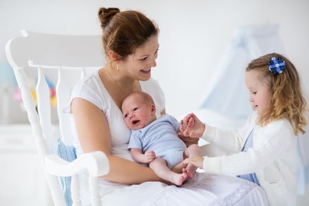 little sister hugging her newborn brother. toddler kid meeting new sibling. mother and new born baby boy relax in a white bedroom. family with children at home. love, trust and tenderness concept.