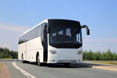 white coach bus on the road in the summer.